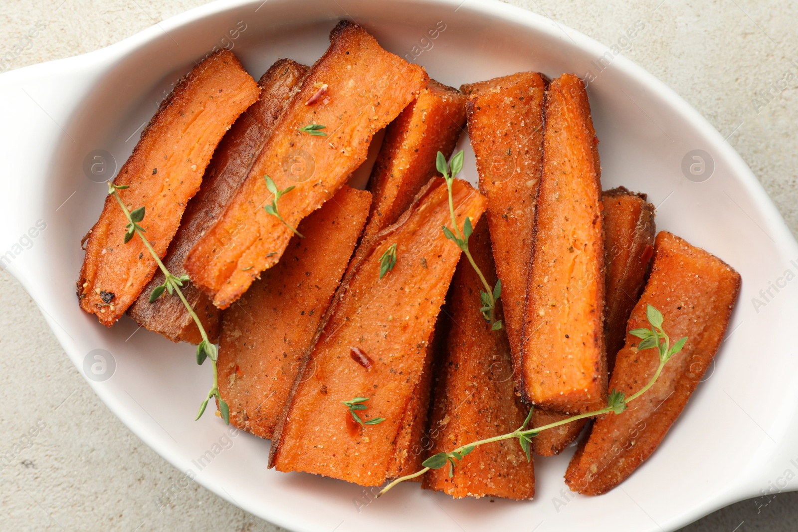 Photo of Pieces of tasty cooked sweet potato with microgreens in baking dish on light textured table, top view