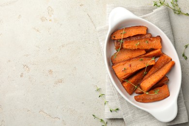 Photo of Pieces of tasty cooked sweet potato in baking dish with microgreens on light textured table, top view. Space for text