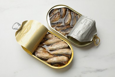 Photo of Tasty sprats in tin cans on white marble table, top view