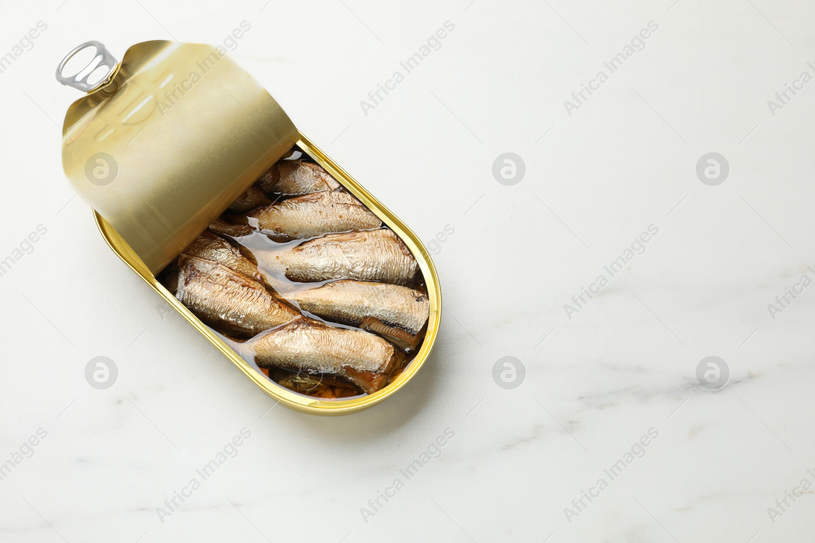 Photo of Tasty sprats in tin can on white marble table, top view. Space for text