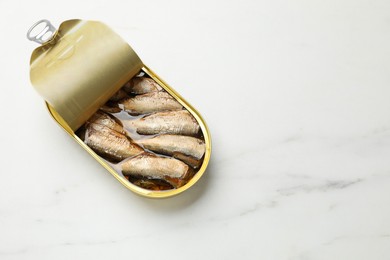 Photo of Tasty sprats in tin can on white marble table, top view. Space for text