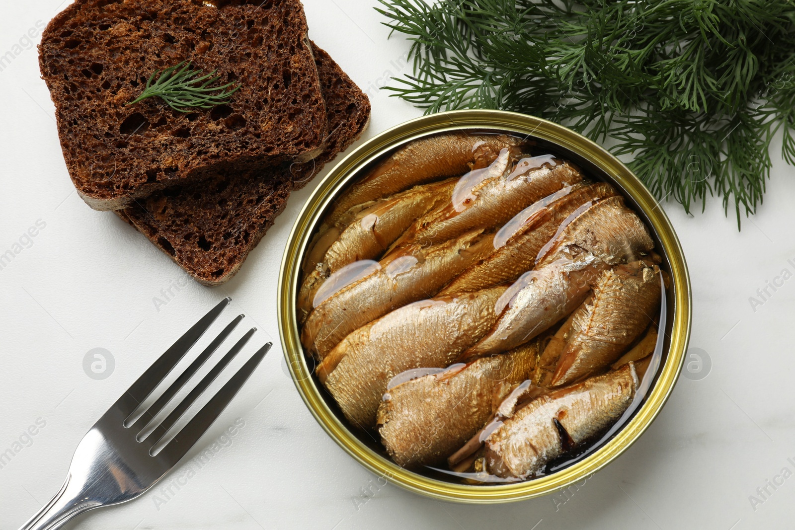 Photo of Tasty sprats in tin can, dill, bread and fork on white marble table, top view