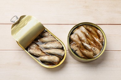 Photo of Tasty sprats in tin cans on wooden table, top view