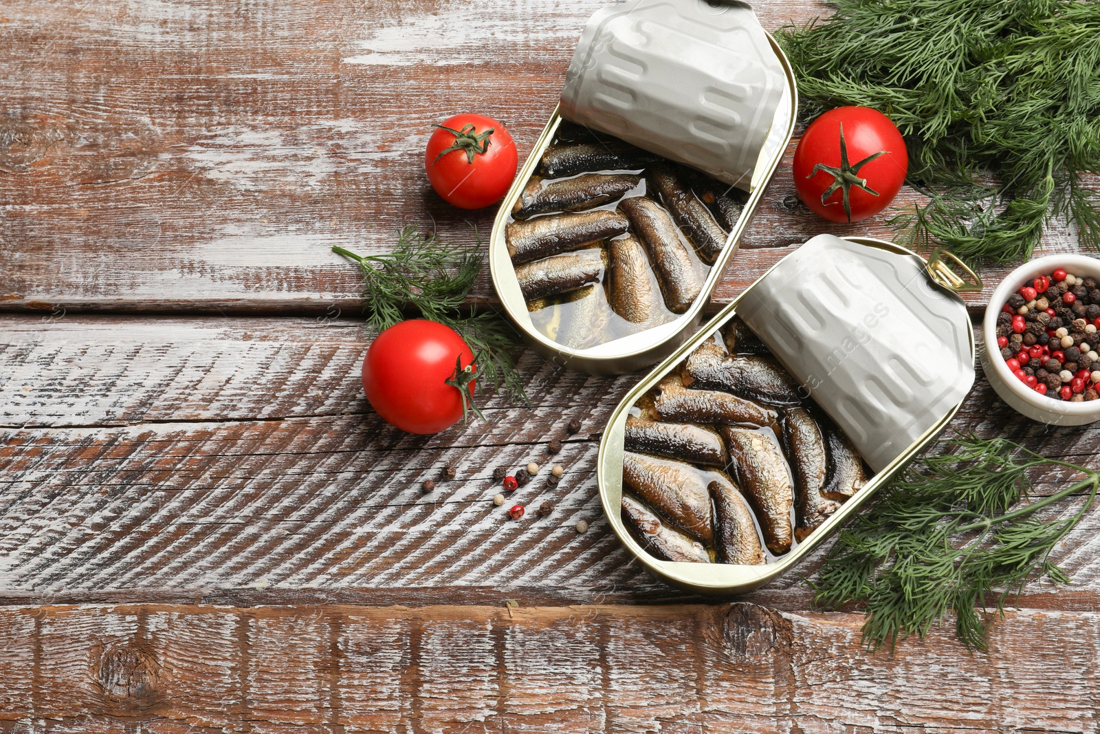 Photo of Tasty sprats in tin cans served on wooden table, flat lay. Space for text