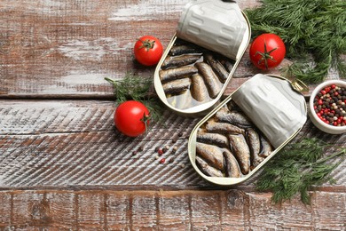 Tasty sprats in tin cans served on wooden table, flat lay. Space for text