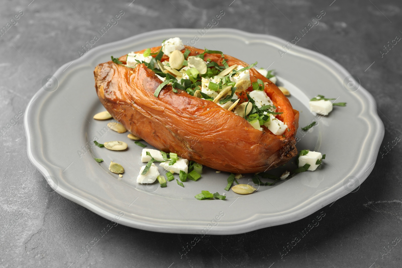 Photo of Tasty cooked sweet potato with feta cheese, pumpkin seeds and green onion on grey table, closeup