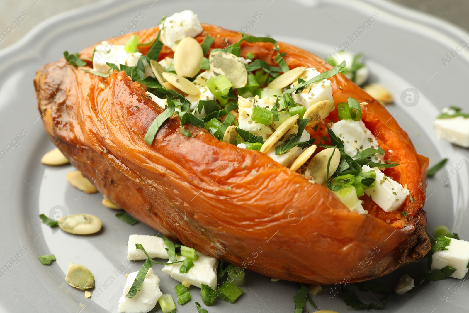 Photo of Tasty cooked sweet potato with feta cheese, pumpkin seeds and green onion on table, closeup