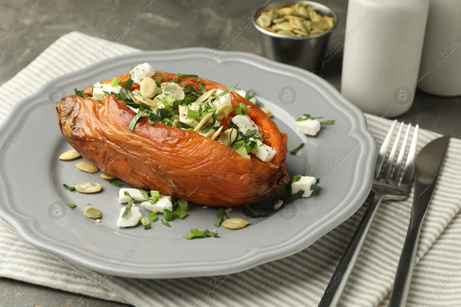 Photo of Tasty cooked sweet potato with feta cheese, pumpkin seeds and green onion on table, closeup