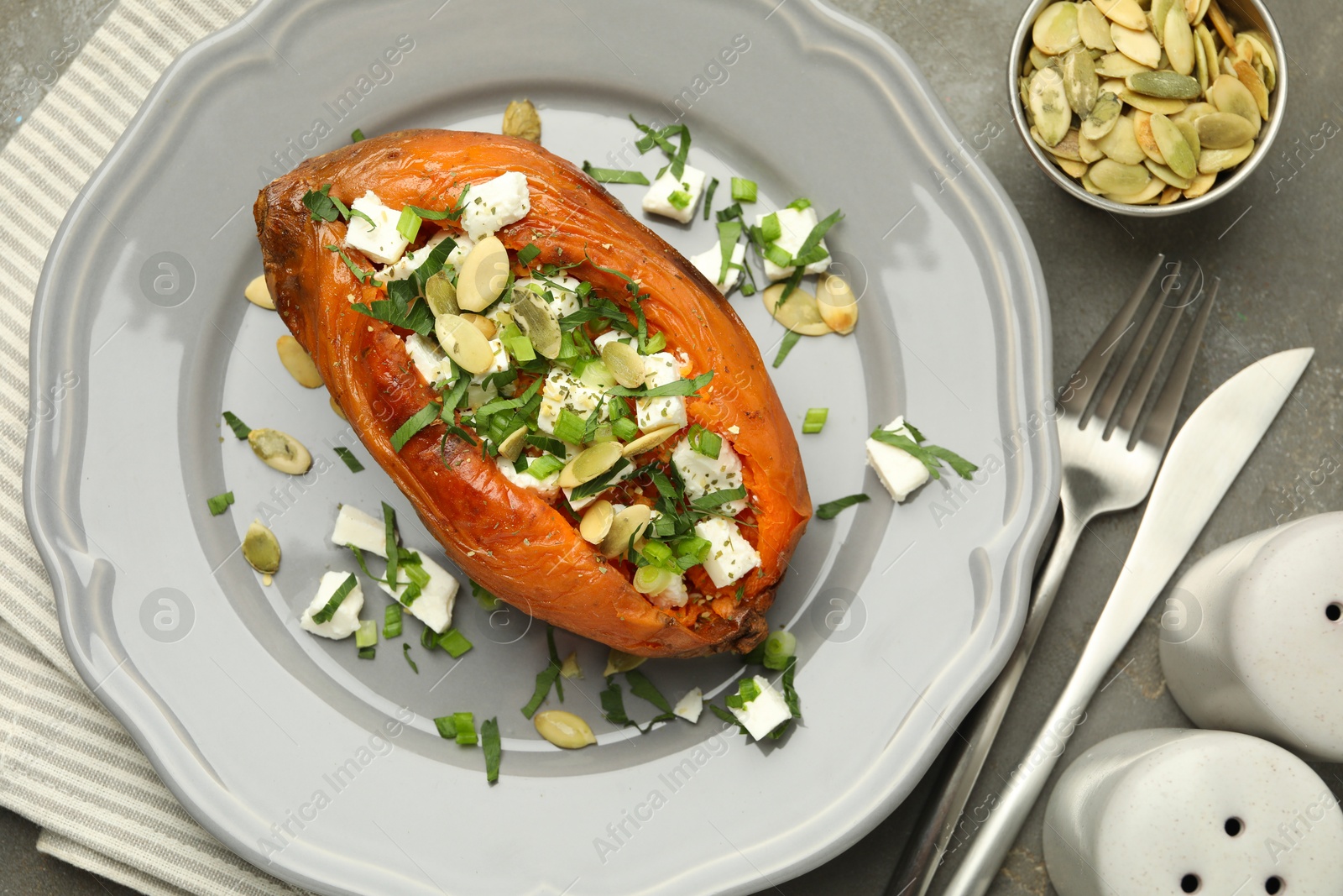 Photo of Tasty cooked sweet potato with feta cheese, pumpkin seeds and green onion on grey table, top view