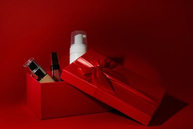 Photo of Christmas gift box with cosmetic products on red background