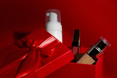 Photo of Christmas gift box with cosmetic products on red background, closeup