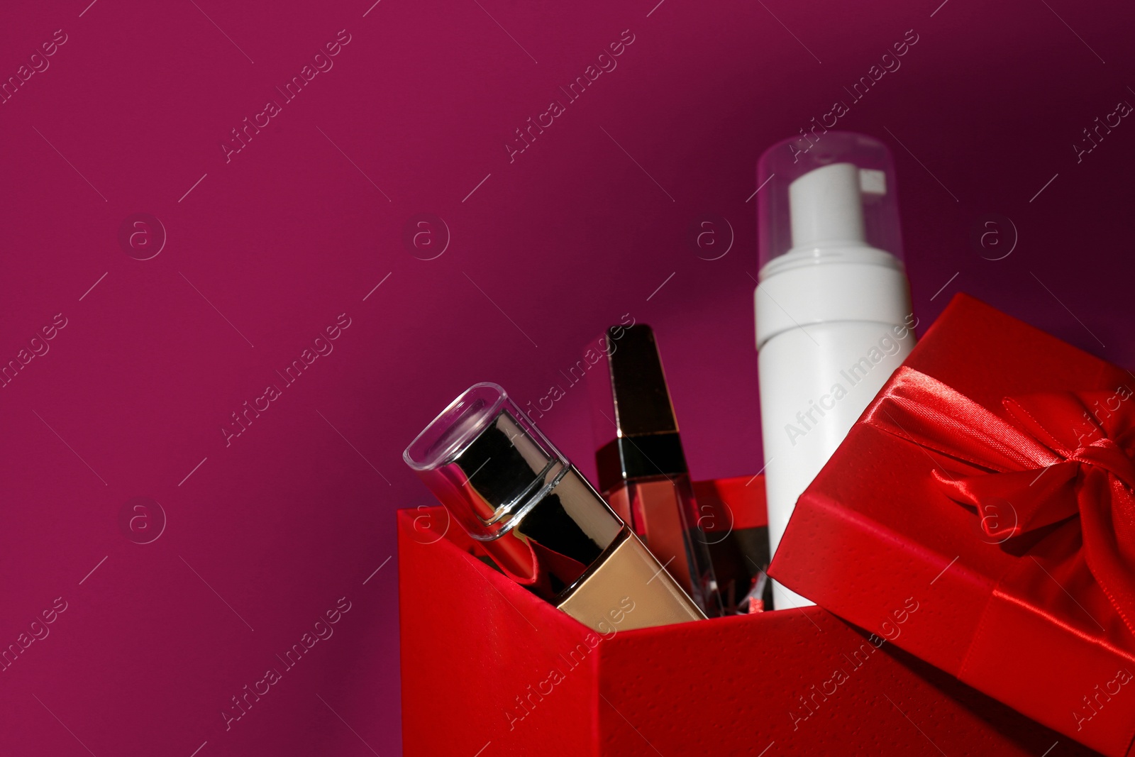 Photo of Christmas gift box with cosmetic products on red background, closeup. Space for text