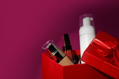 Photo of Christmas gift box with cosmetic products on red background, closeup. Space for text