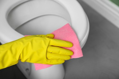 Photo of Woman cleaning toilet seat in restroom, closeup