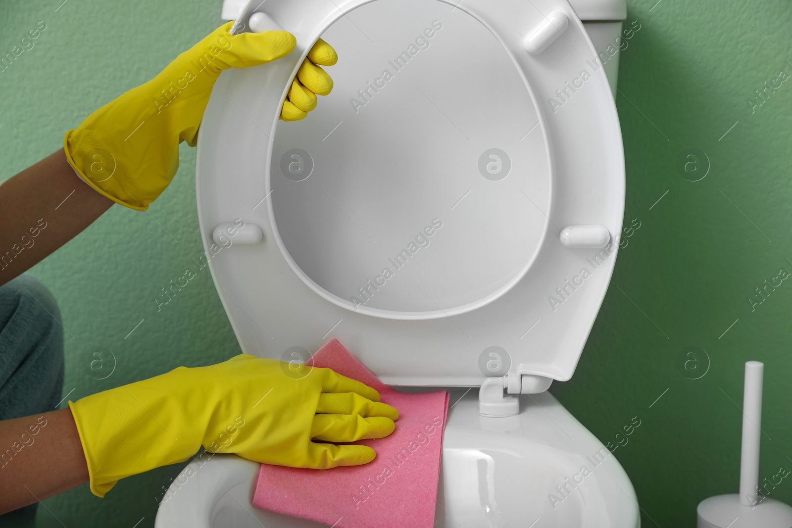 Photo of Woman cleaning toilet seat in restroom, closeup