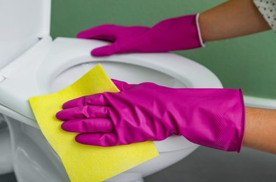 Photo of Woman cleaning toilet seat in restroom, closeup