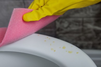 Photo of Woman wiping urine drops from toilet seat in restroom, closeup