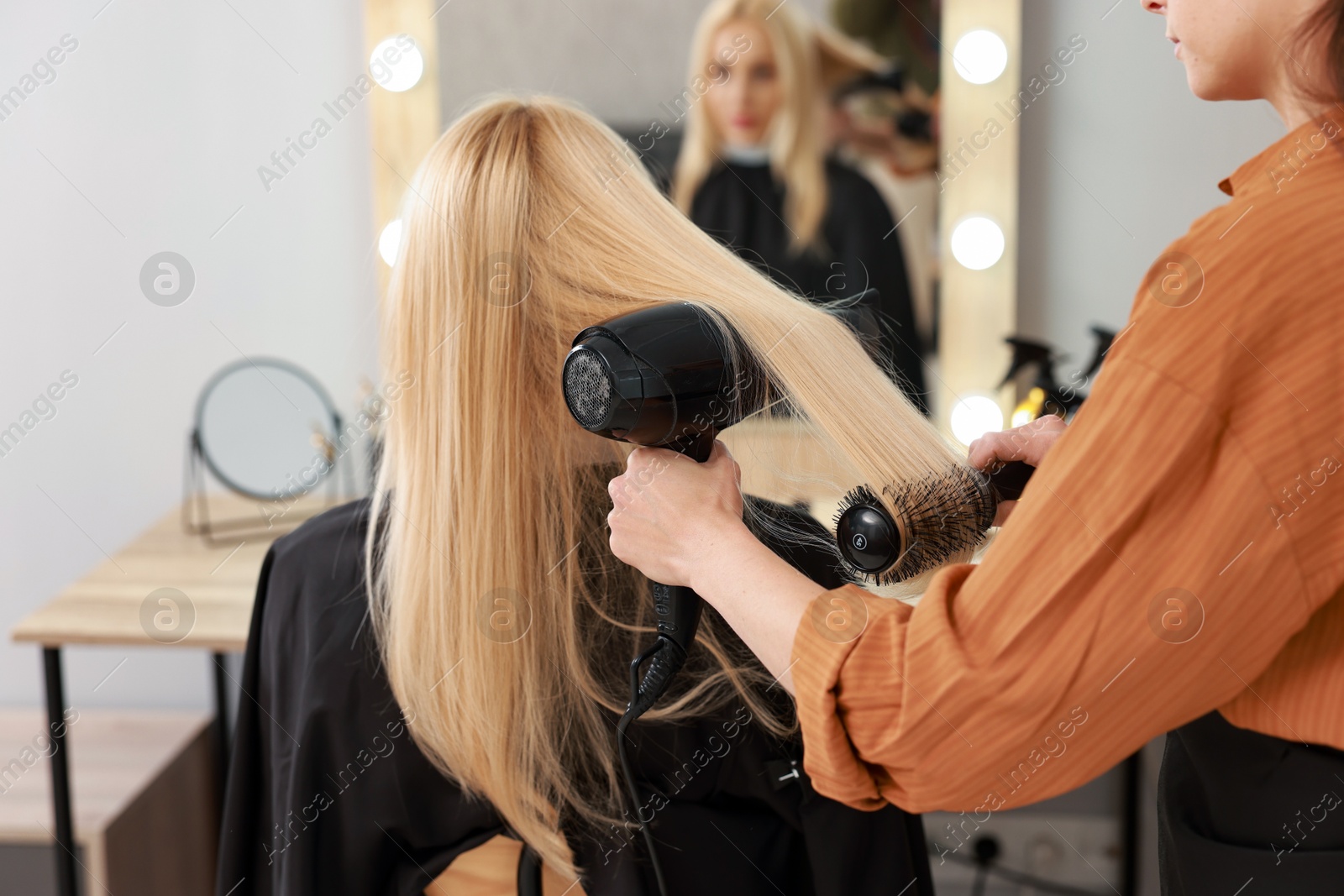 Photo of Hairdresser blow drying client's hair in salon, closeup