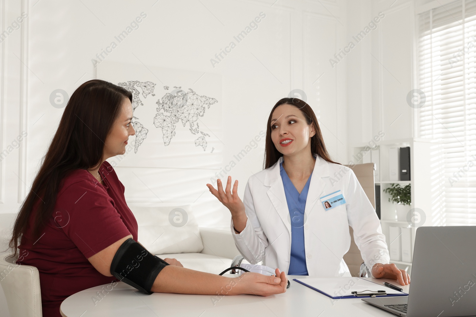 Photo of Nutritionist measuring overweight woman's blood pressure at desk in hospital