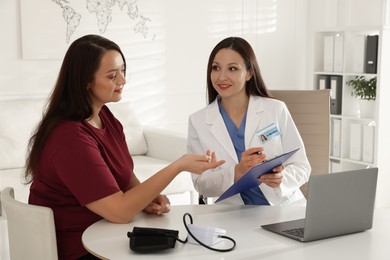 Photo of Overweight woman having consultation with nutritionist at desk in clinic