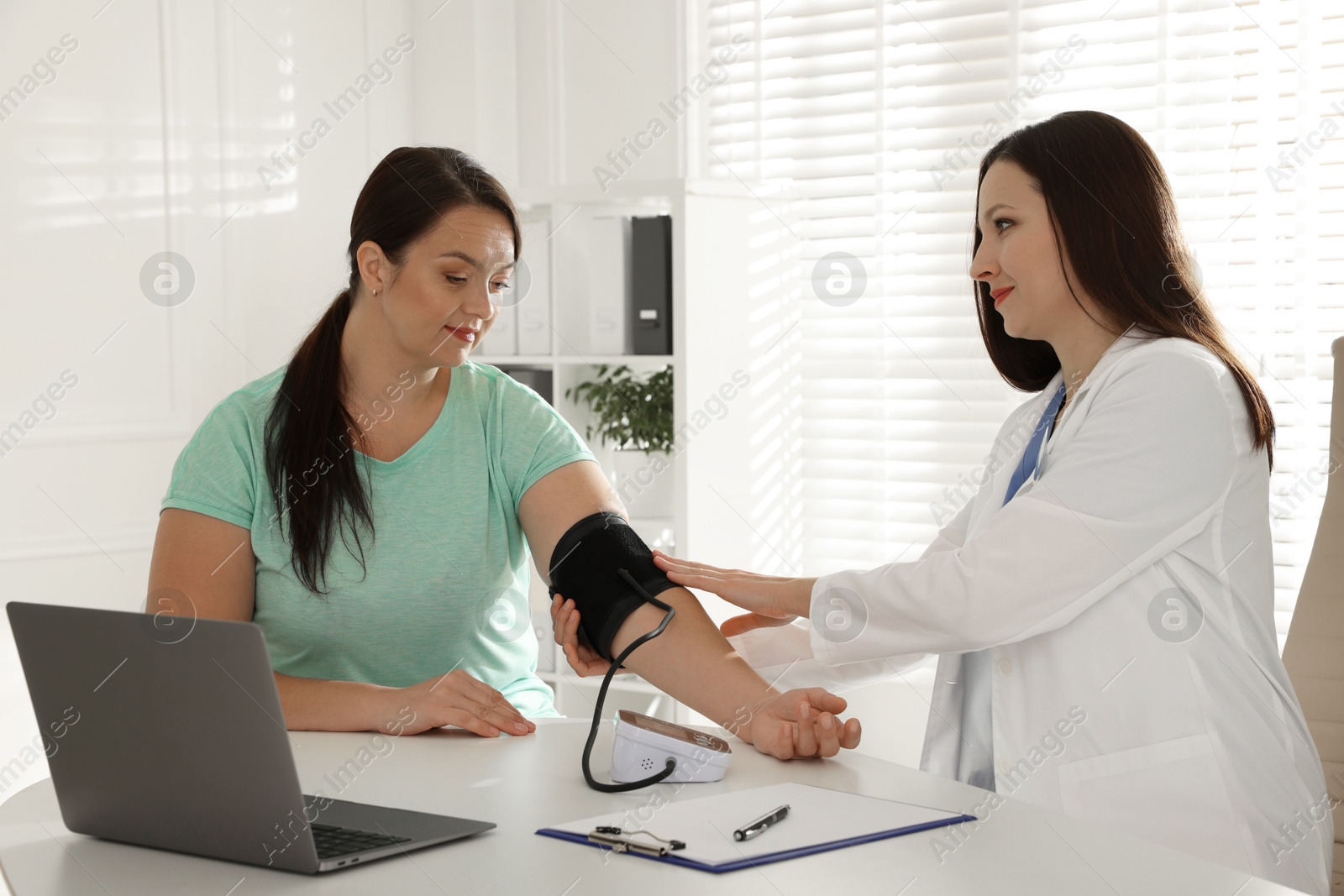 Photo of Nutritionist measuring overweight woman's blood pressure at desk in hospital