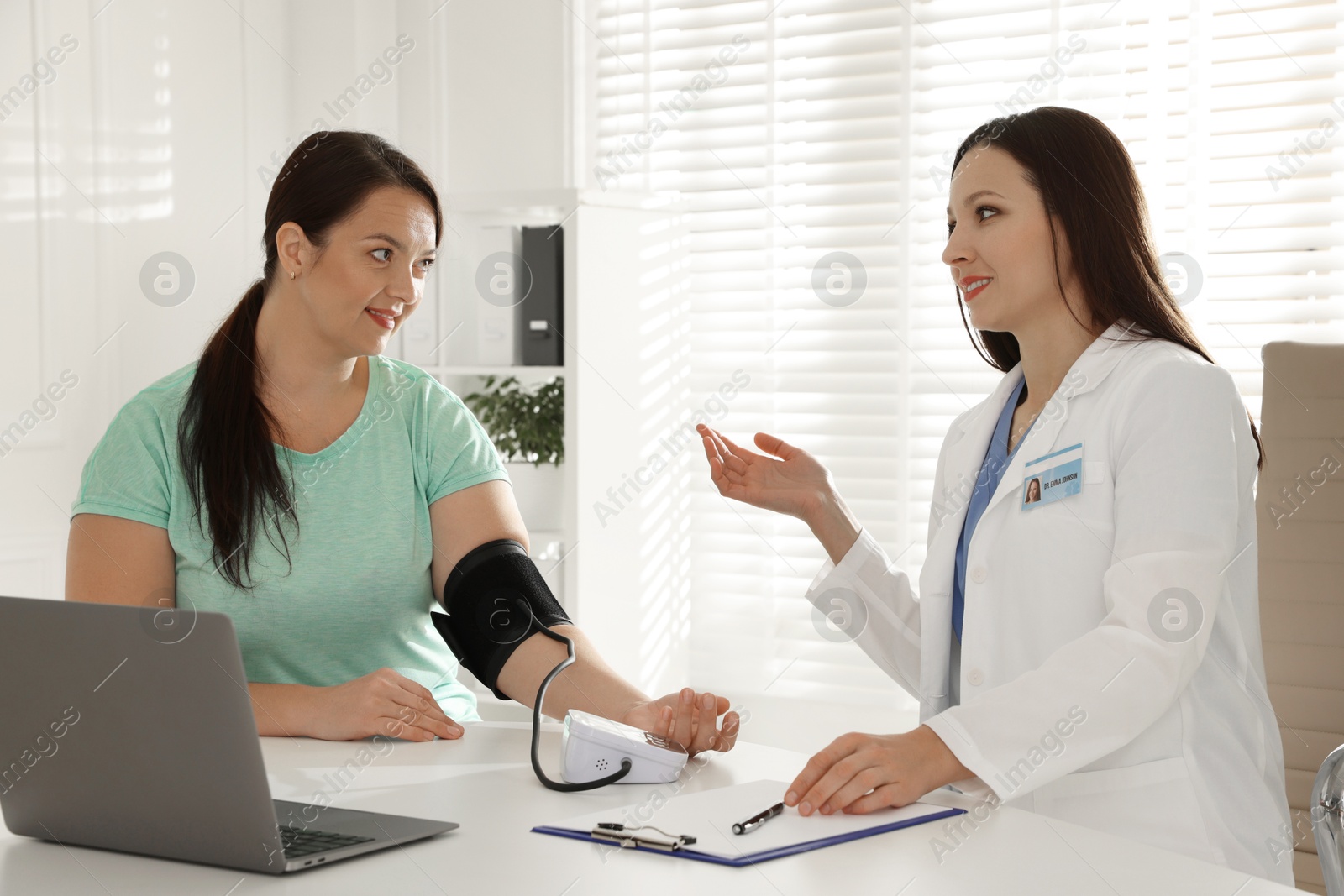 Photo of Nutritionist measuring overweight woman's blood pressure at desk in hospital