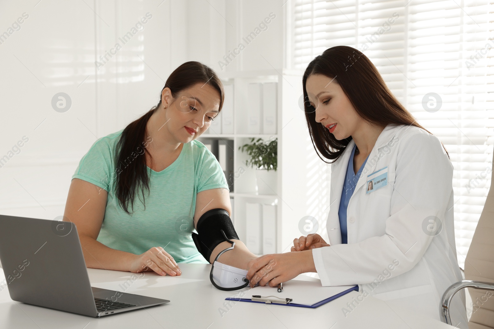 Photo of Nutritionist measuring overweight woman's blood pressure at desk in hospital