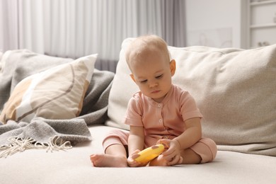 Photo of Cute little baby with rattle on sofa indoors