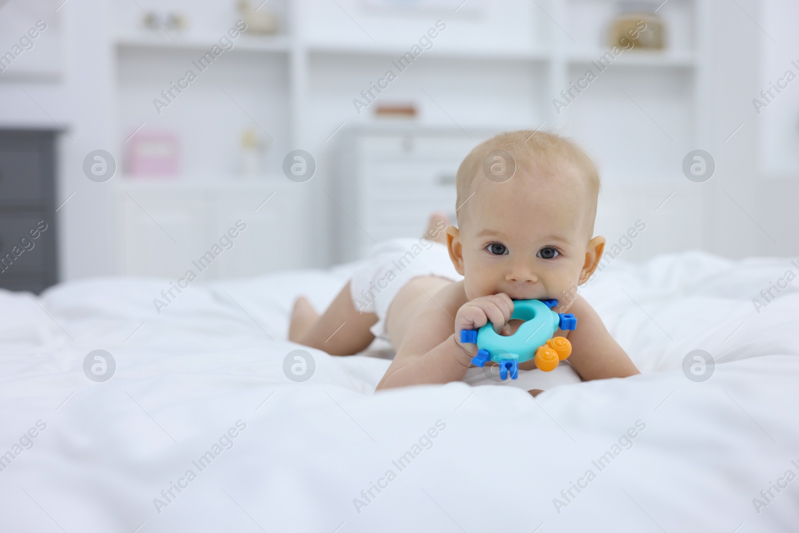 Photo of Cute little baby with rattle on bed indoors, space for text