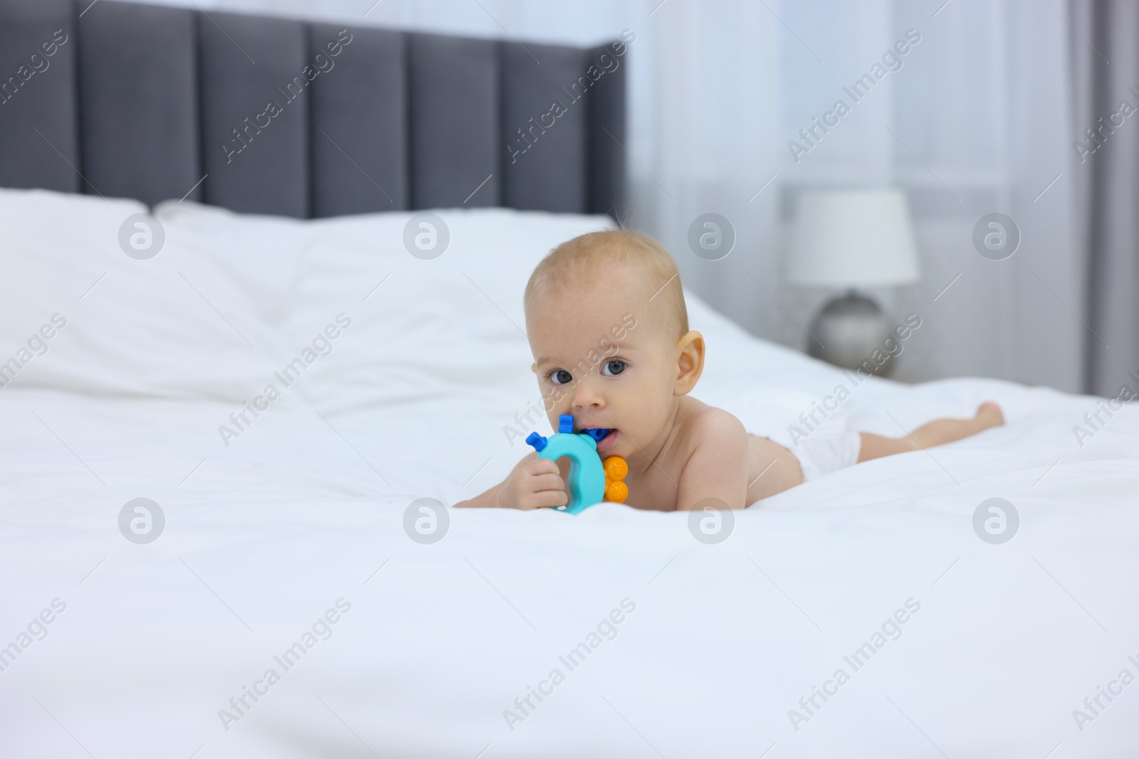 Photo of Cute little baby with rattle on bed indoors