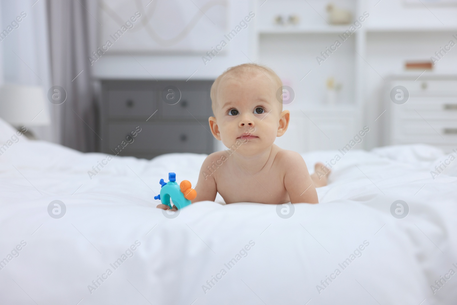 Photo of Cute little baby with rattle on bed indoors