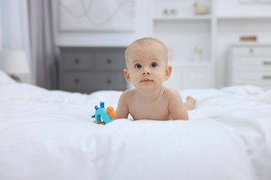 Photo of Cute little baby with rattle on bed indoors