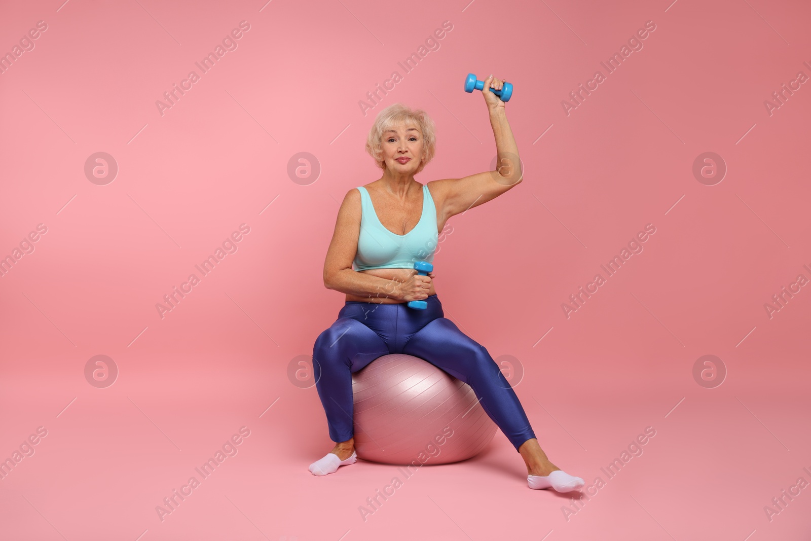 Photo of Senior woman exercising with fitness mat and dumbbells on pink background