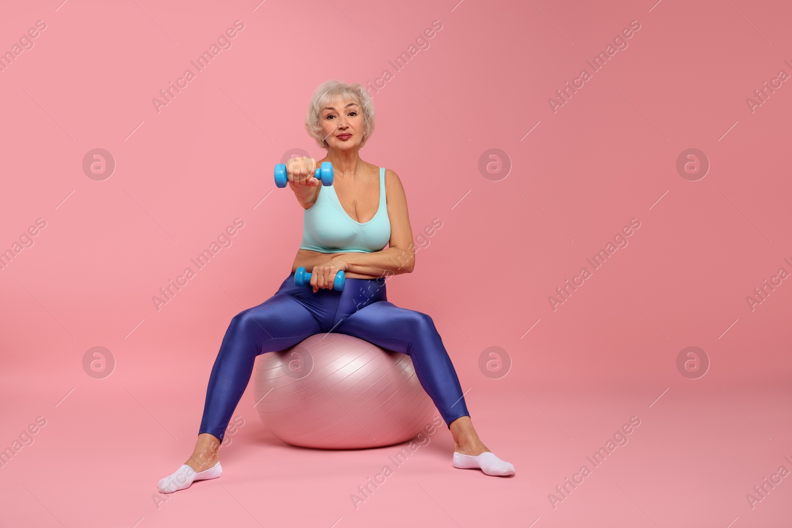 Photo of Senior woman exercising with fitness mat and dumbbells on pink background