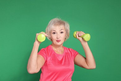 Photo of Senior woman exercising with dumbbells on green background