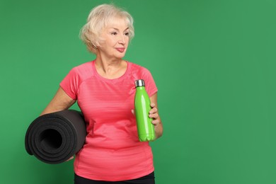 Photo of Senior woman with fitness mat and water on green background, space for text