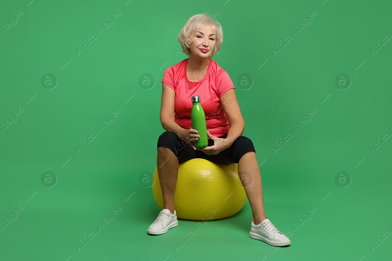 Photo of Senior woman with fitness ball and water on green background