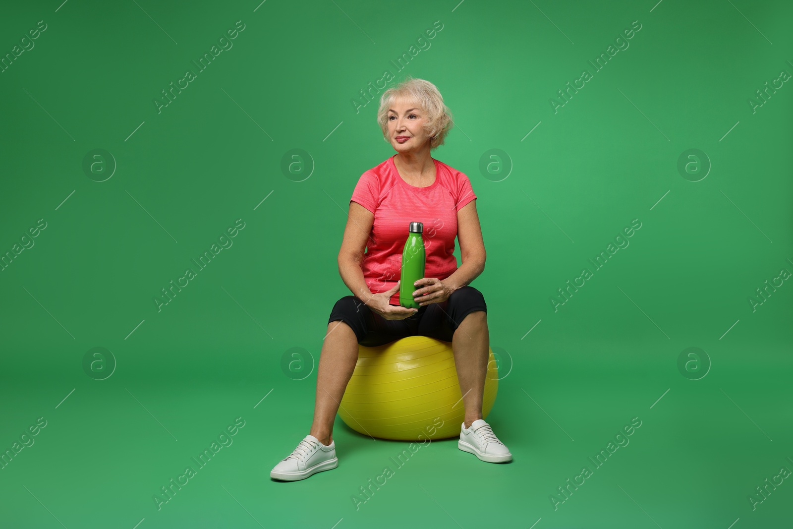 Photo of Senior woman with fitness ball and water on green background