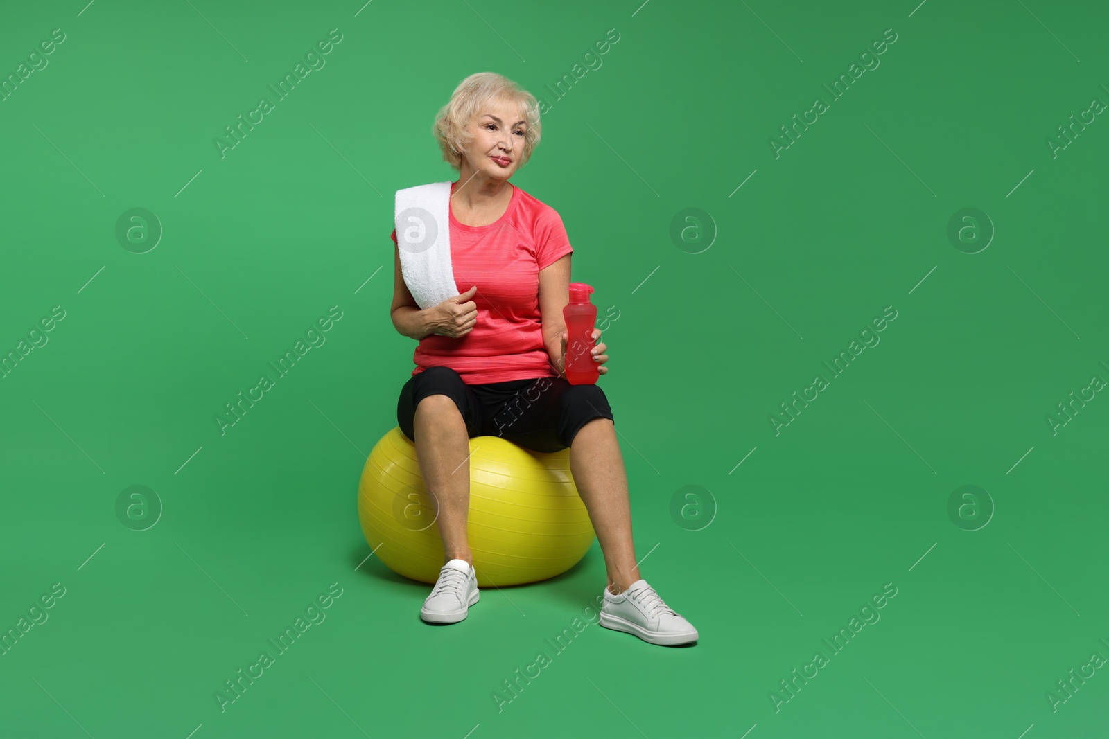 Photo of Senior woman with fitness ball, water and towel on green background