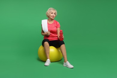 Photo of Senior woman with fitness ball, water and towel on green background