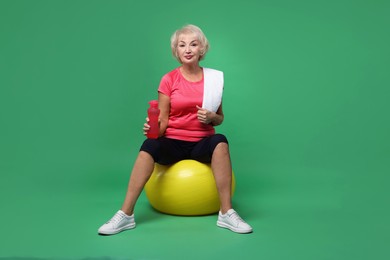 Photo of Senior woman with fitness ball, water and towel on green background