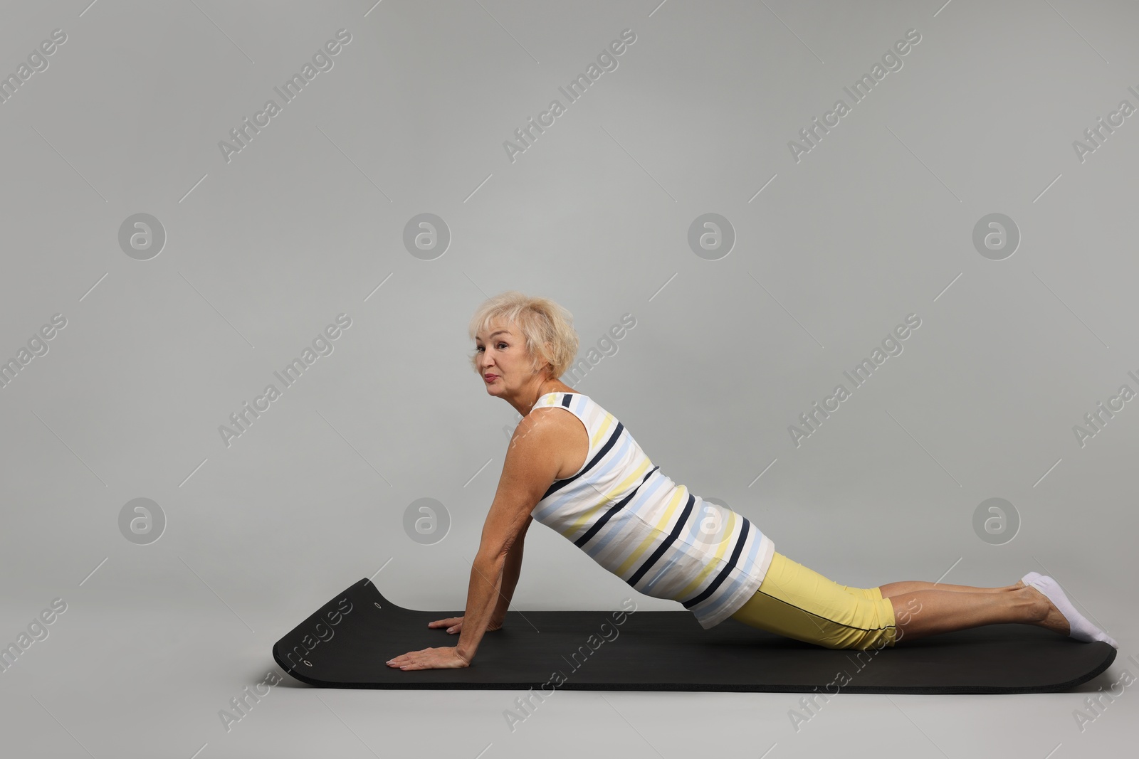 Photo of Senior woman exercising with fitness mat on light grey background