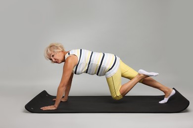 Photo of Senior woman exercising with fitness mat on light grey background