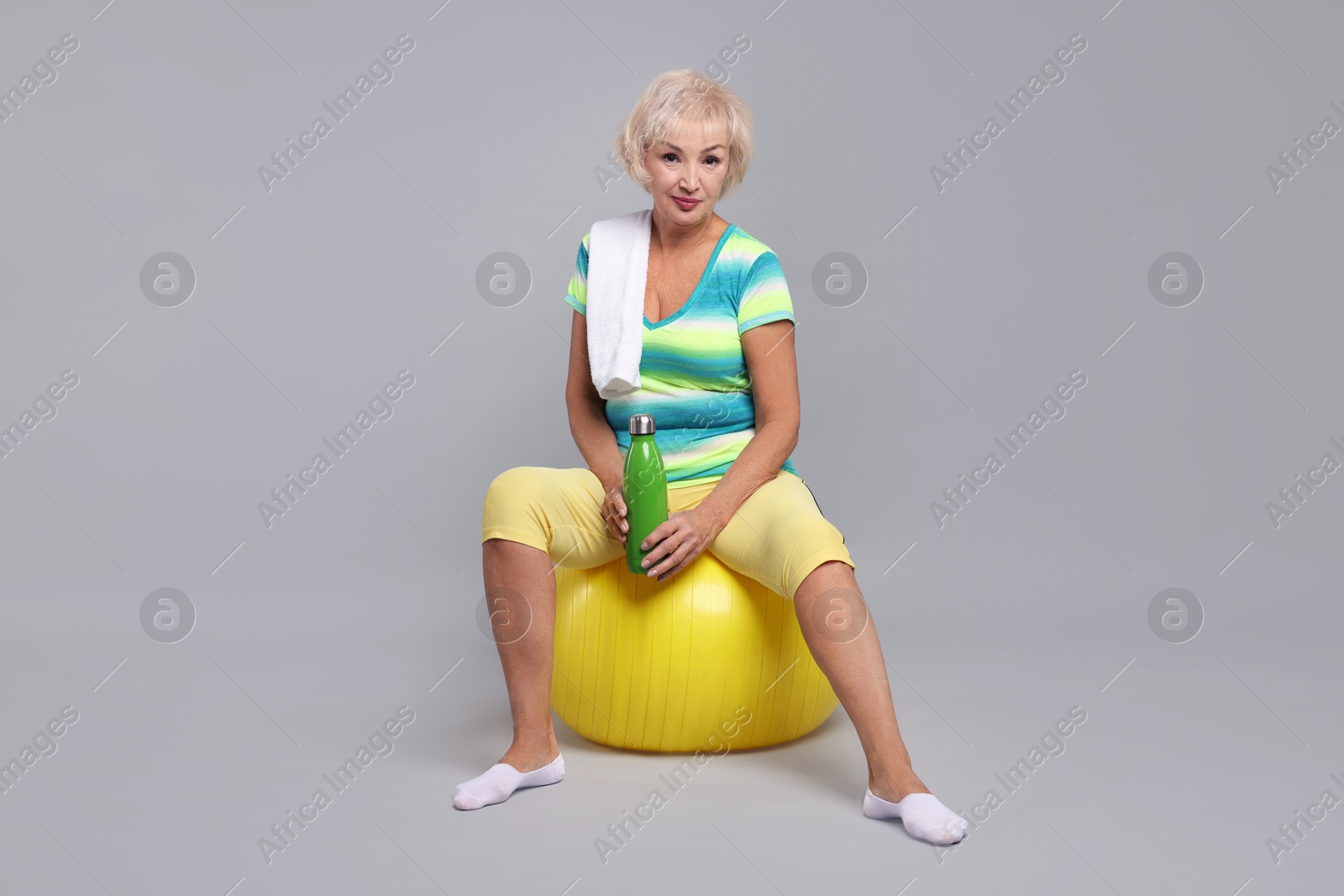 Photo of Senior woman with fitness ball, water and towel on light grey background