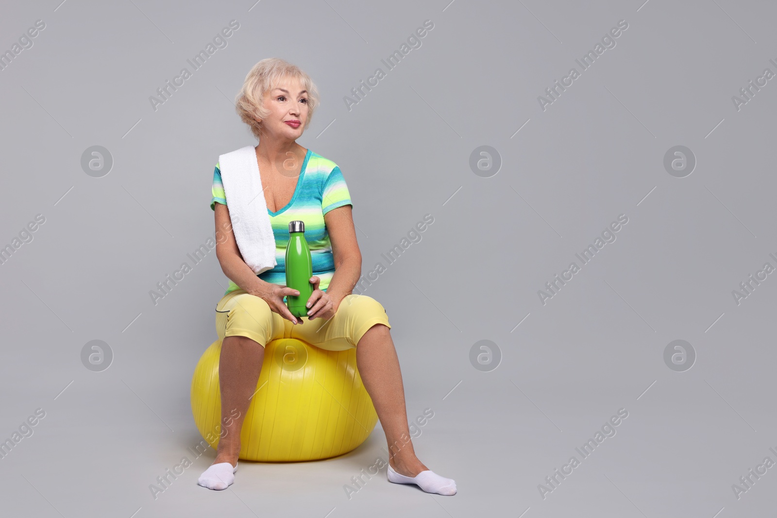 Photo of Senior woman with fitness ball, water and towel on light grey background, space for text