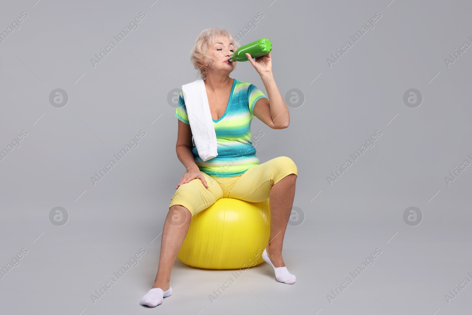 Photo of Senior woman with fitness ball, water and towel on light grey background