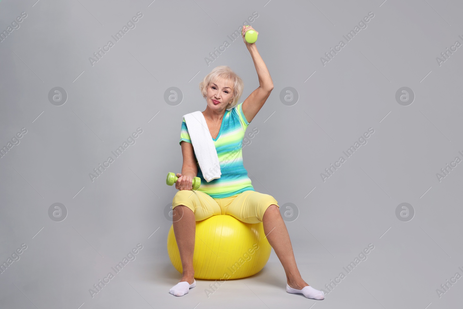 Photo of Senior woman exercising with fitness ball, dumbbells and towel on light grey background