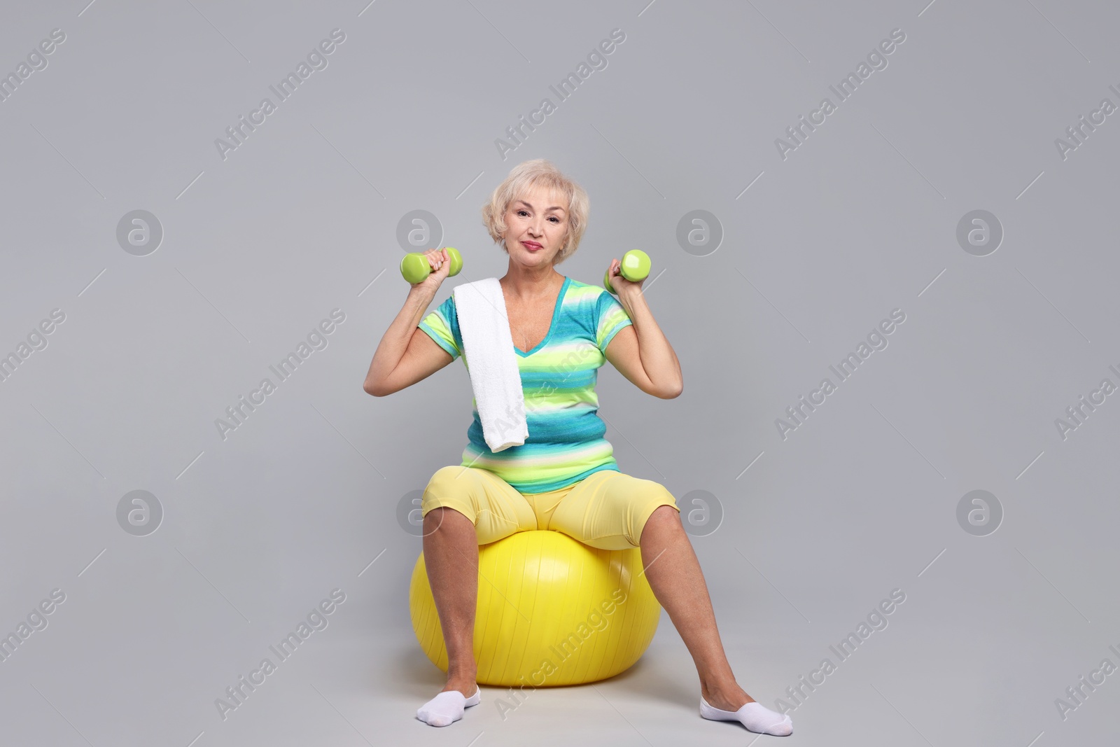 Photo of Senior woman exercising with fitness ball, dumbbells and towel on light grey background