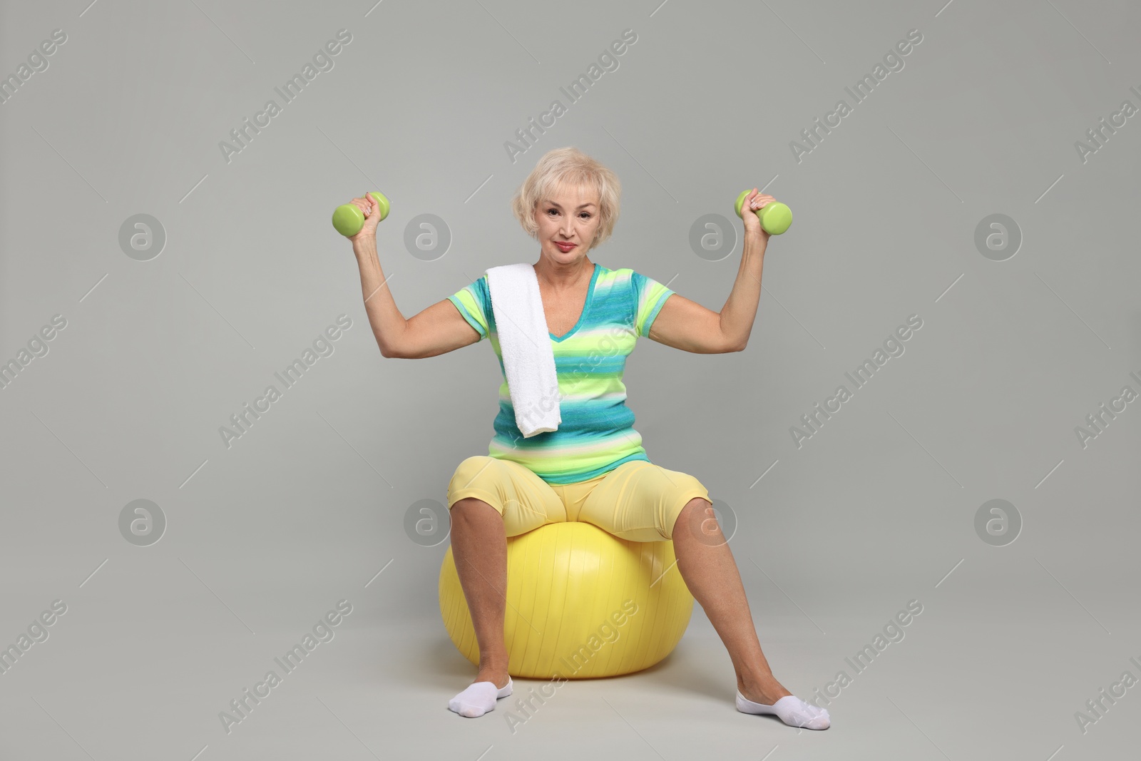 Photo of Senior woman exercising with fitness ball, dumbbells and towel on light grey background