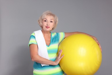 Photo of Senior woman with fitness ball and towel on light grey background